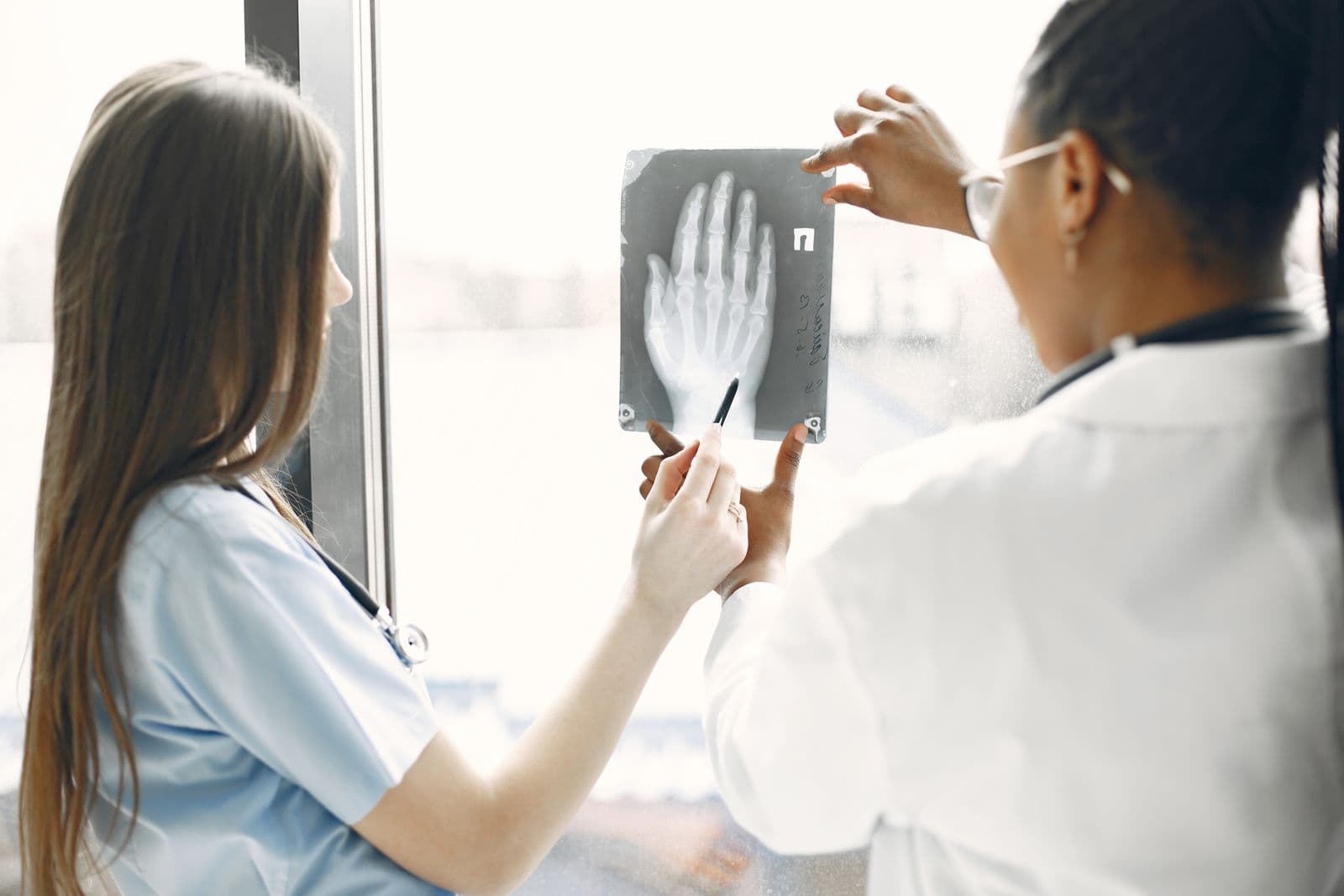 Two clinicians reviewing a hand X-ray beside a bright window