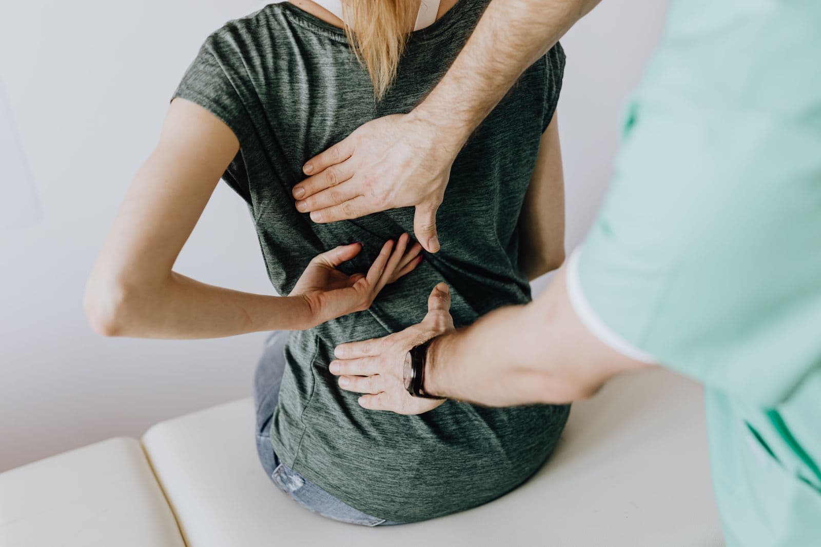 Clinician in teal scrubs examining a patient's back in a bright treatment room